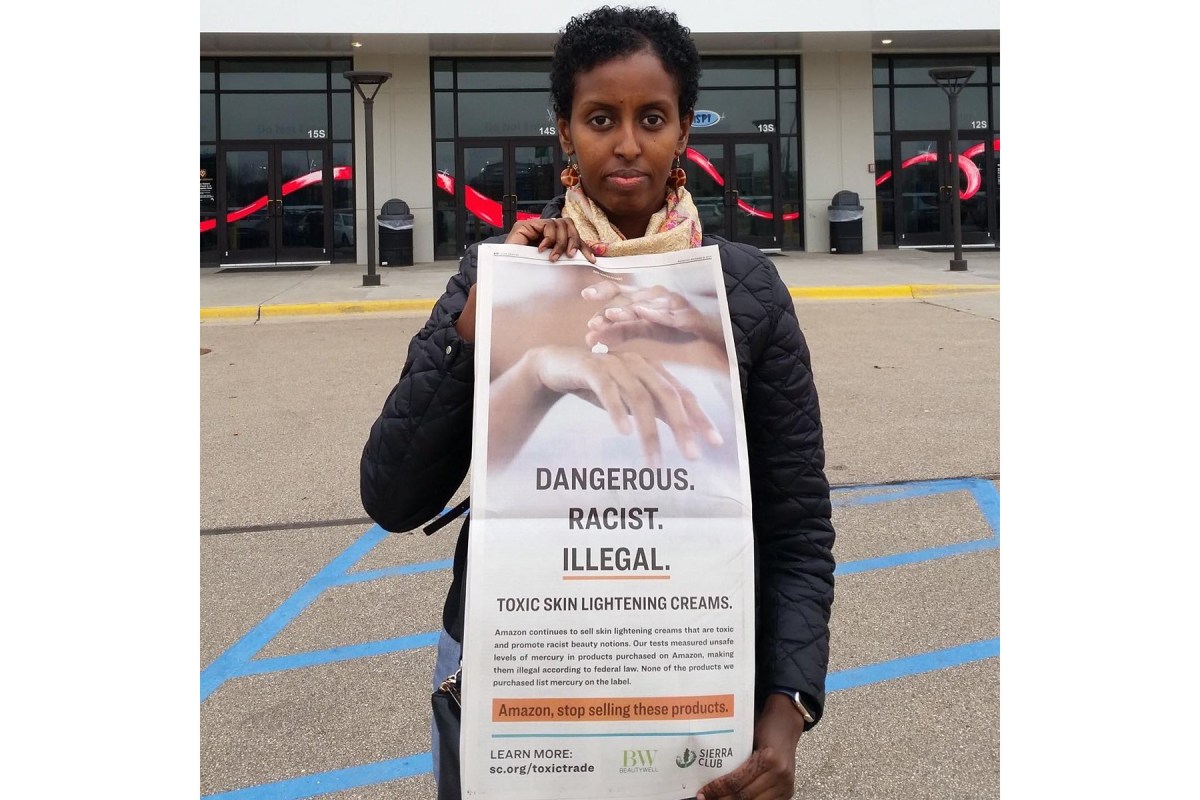 Image of Amira Adawe standing outside and holding a poster that reads "Dangerous. Racist. Illegal. Toxic skin lightening creams."